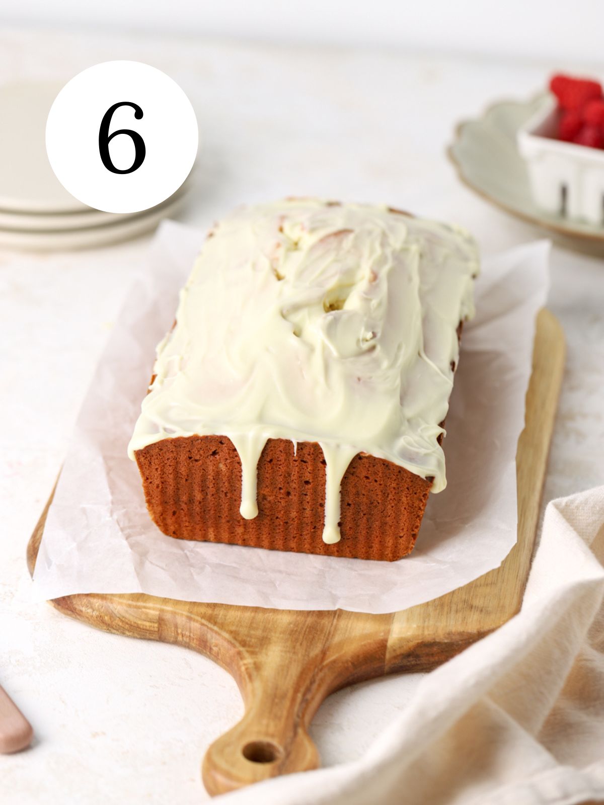 A raspberry loaf cake topped with white chocolate on parchment paper.