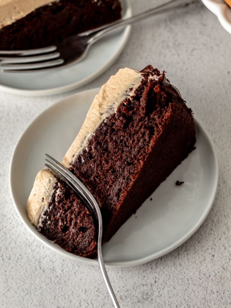 A close up of a piece of chocolate cake on a plate with a fork in it. 