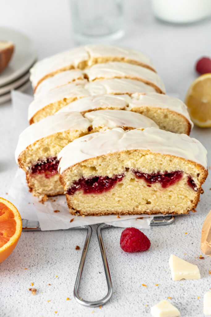 Raspberry cake cut into slices with white chocolate and fruit nearby. 