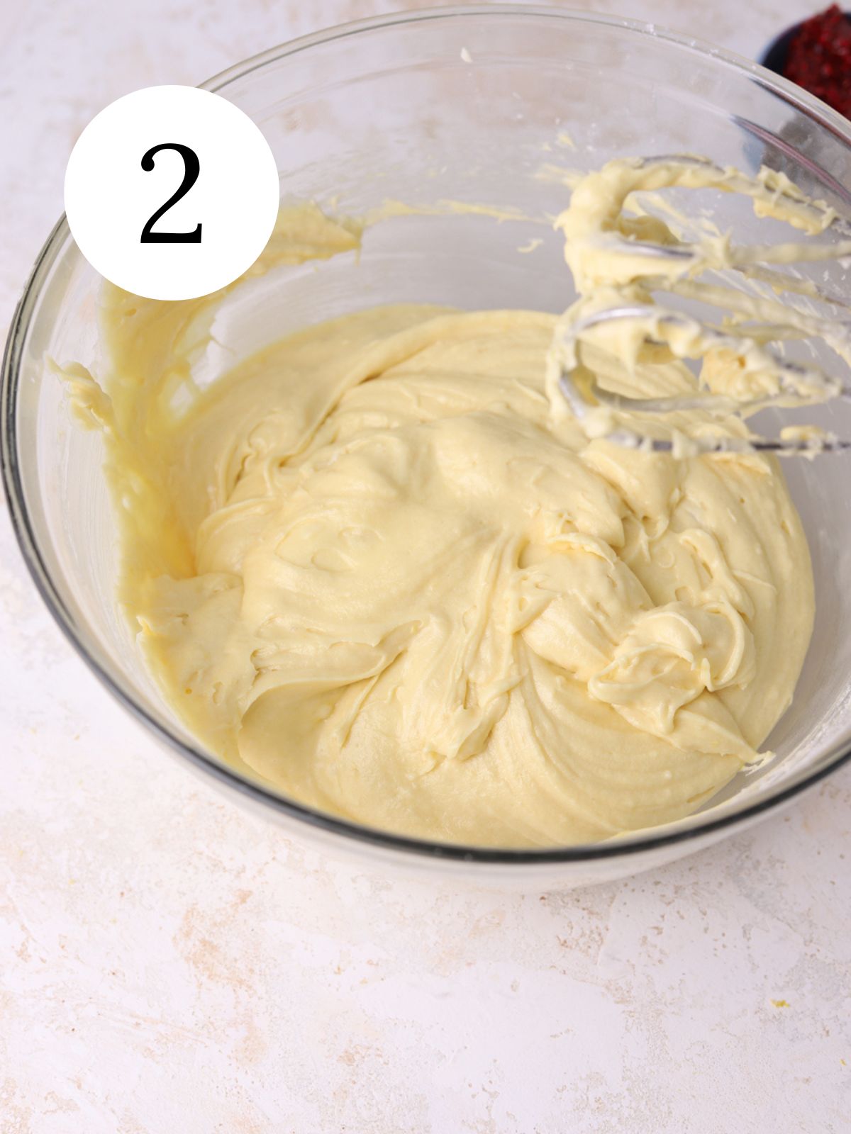 Vanilla cake batter in a large glass mixing bowl with an electric mixer.