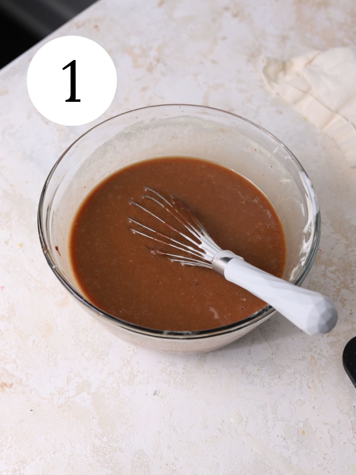 Cake ingredients in a glass bowl with a whisk. 