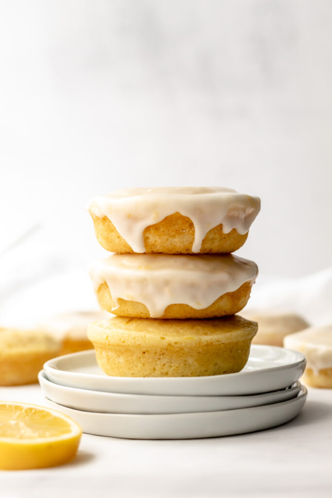 A stack of lemon donuts on three white plates. 