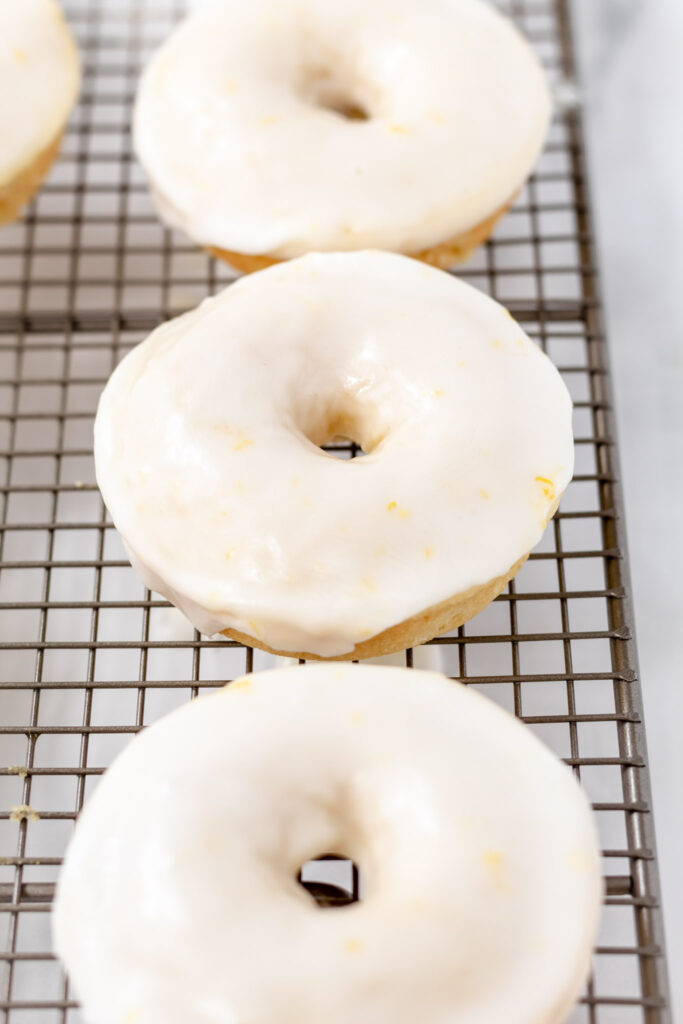 Three lemon donuts covered with thick glaze on a rack.