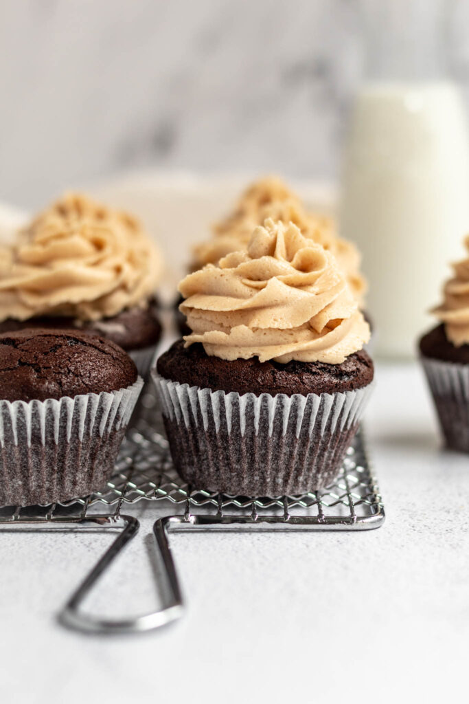Chocolate cupcakes with tall swirls of frosting on a rack. 