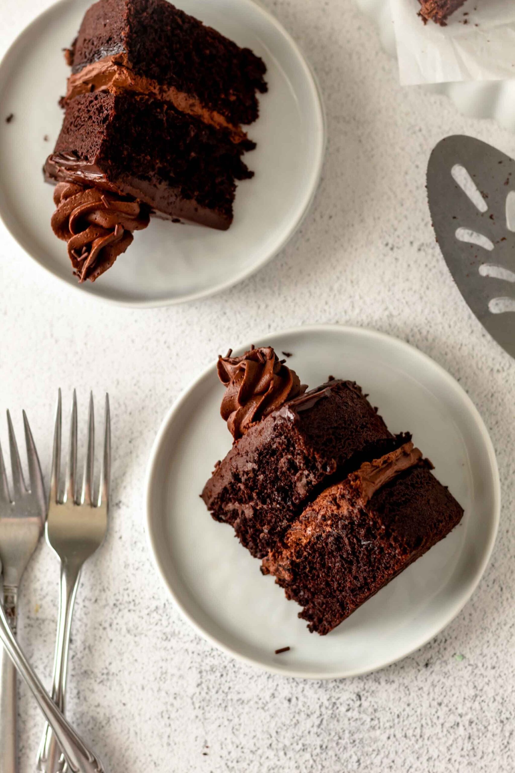 Slices of chocolate cake on small white plates with forks and a spatula nearby.