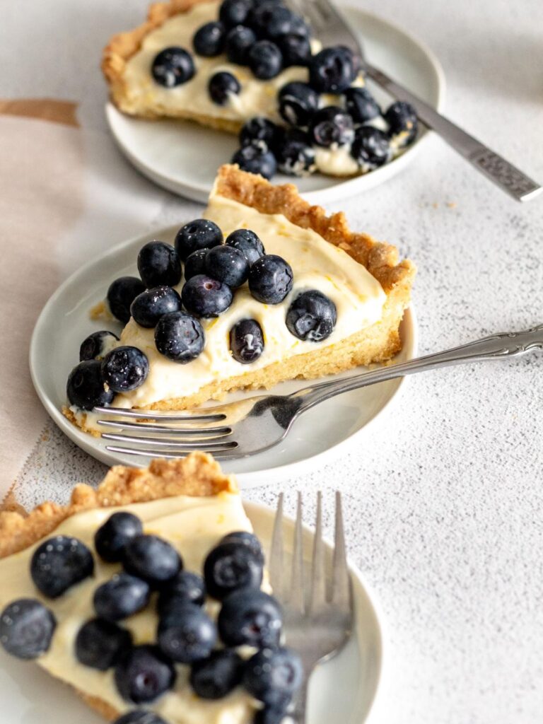 Three slices of mascarpone tart with blueberries on plates. 