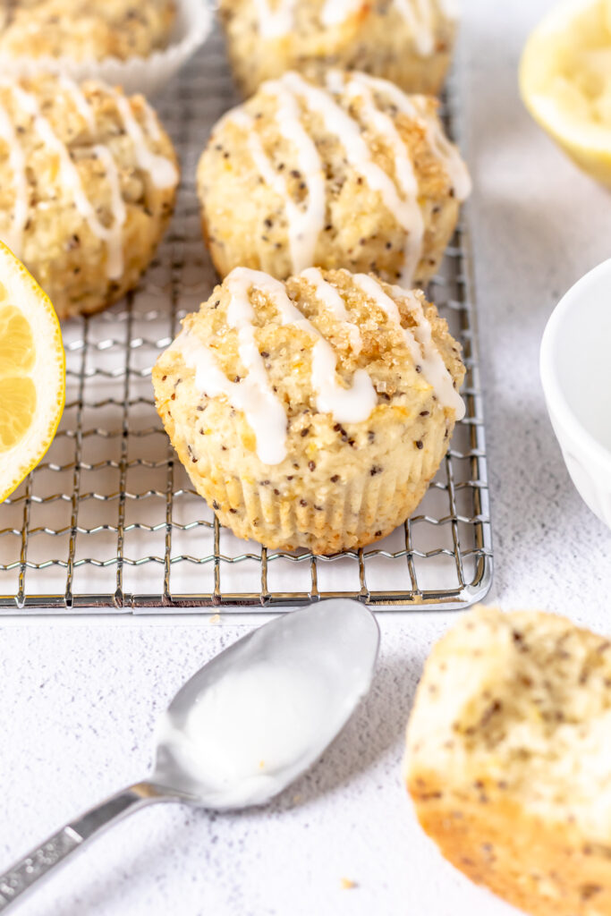 Muffins with chia seeds topped with icing on a rack next to a sliced lemon.