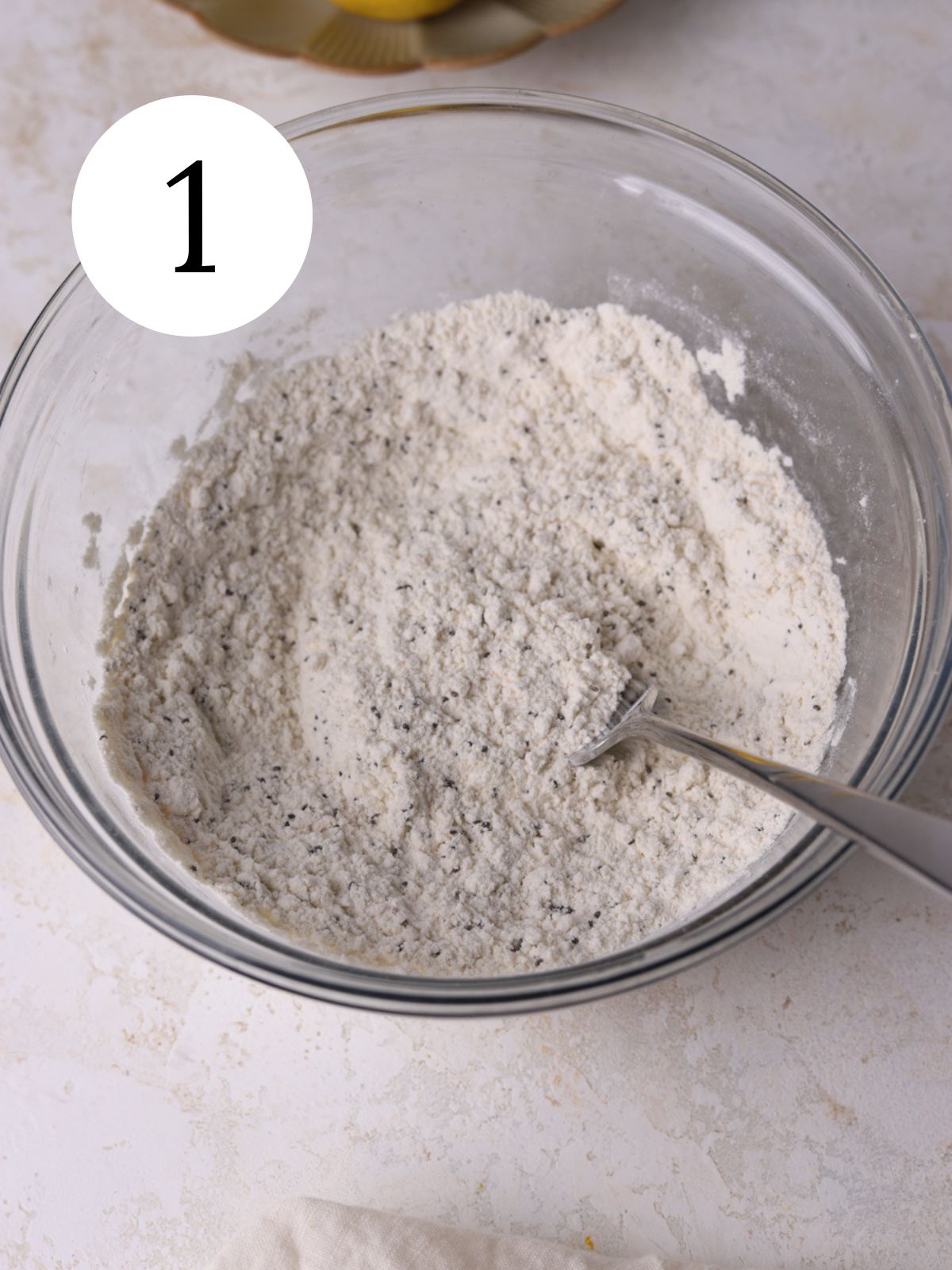 A glass mixing bowl with dry ingredients mixed together with a fork. 