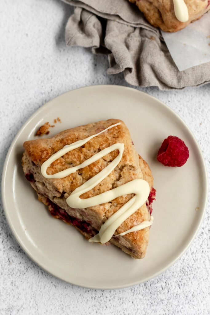 A scone with raspberries inside and white chocolate on top on a plate. 