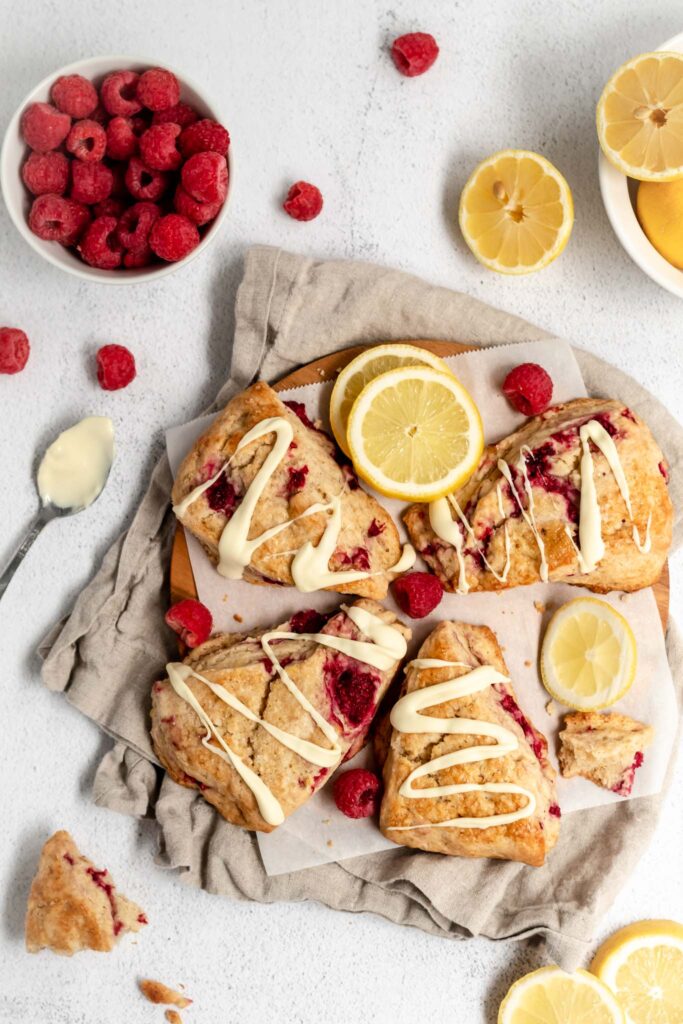 Golden scones on parchment paper with lemon slices and a spoon with white chocolate next to them.