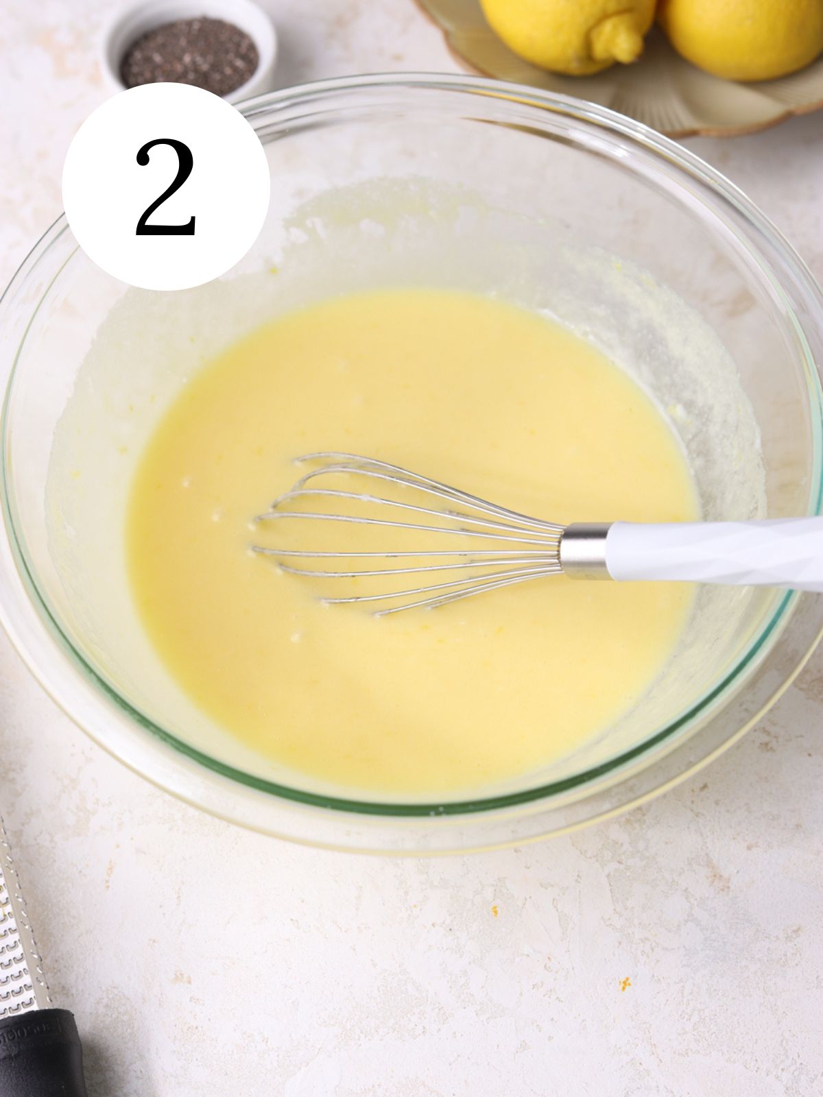 Wet ingredients and a whisk in a glass mixing bowl. 