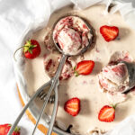 Ice cream in a container topped with strawberries and ice cream scoops.