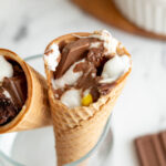 Two ice cream cones filled with melted chocolate and marshmallows in a glass.