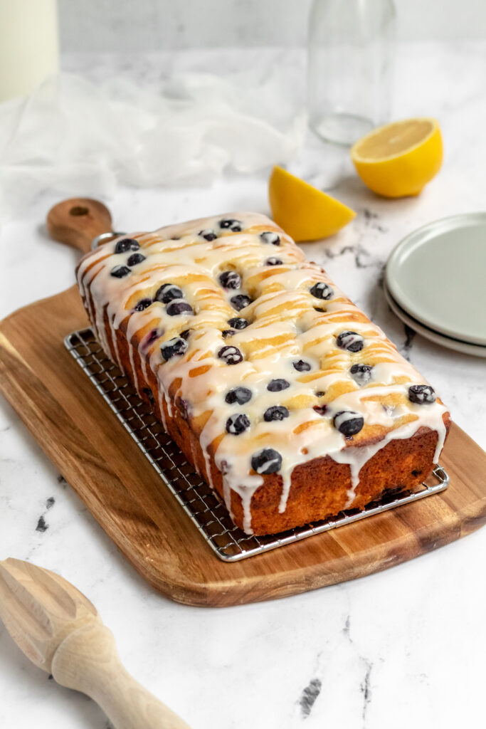 A lemon ricotta pound cake topped with lots of blueberries and icing on a rack. 