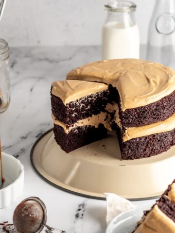 Two layer chocolate cake with frosting and some milk jugs.
