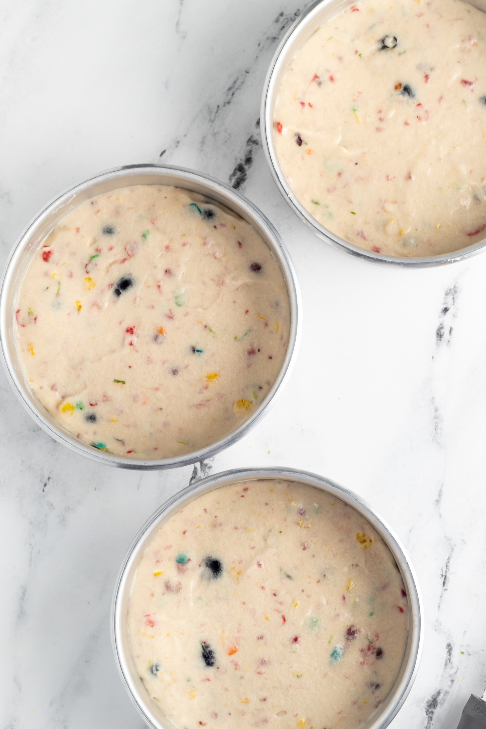 Three cake pans filled with Fruity Pebbles cake batter. 