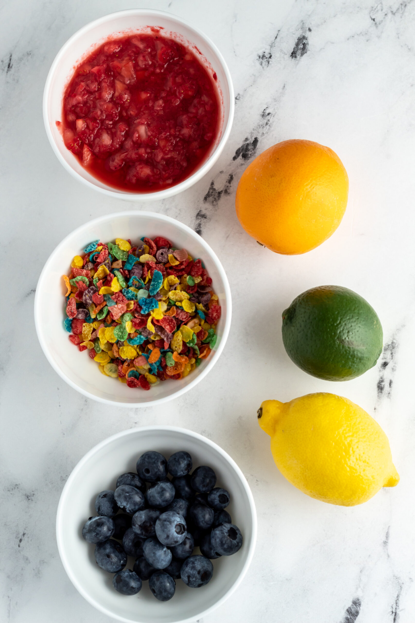 Fruity Pebbles cereal, bowls of strawberries and blueberries and citrus fruit.