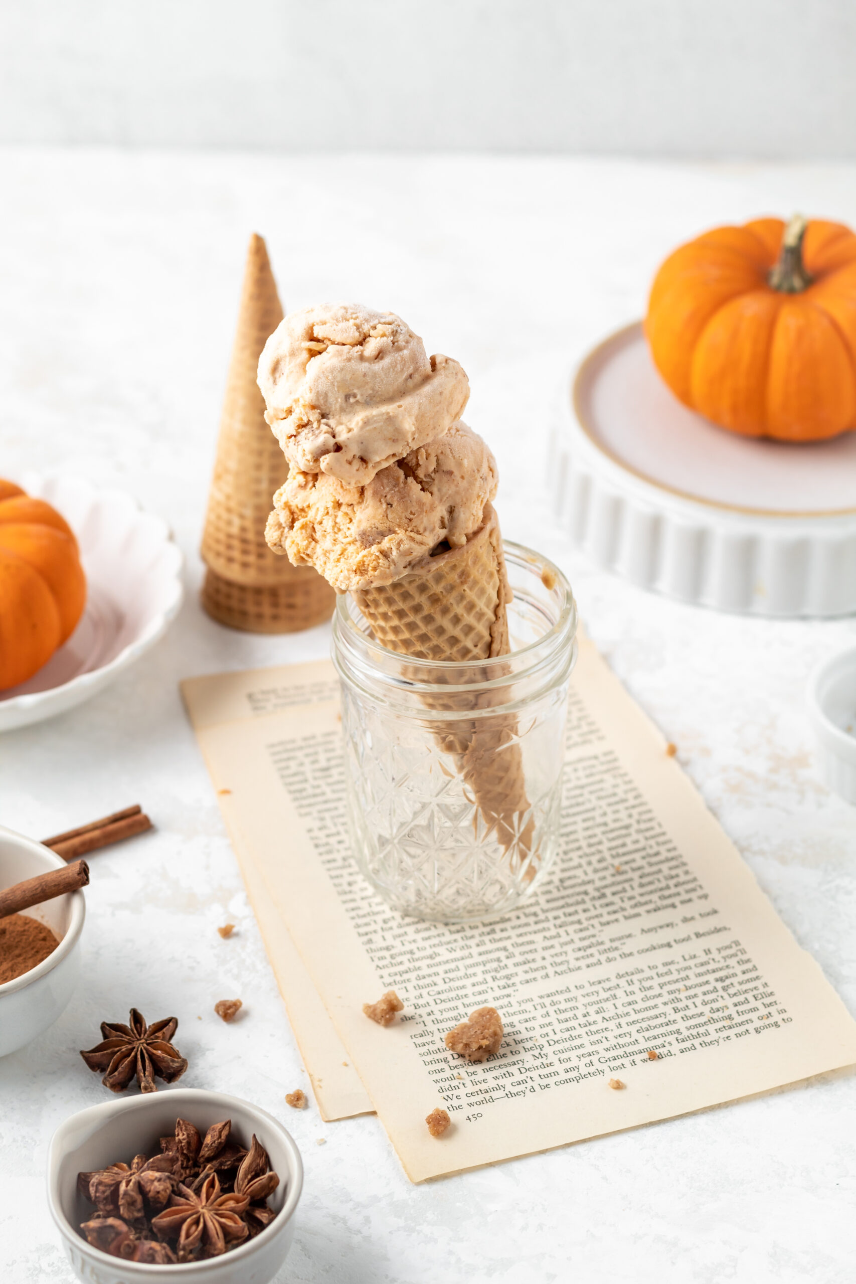 A pumpkin ice cream cone and some tiny pumpkins and spices nearby.