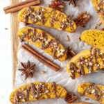 Orange pumpkin biscotti with chocolate on top with some cinnamon sticks on parchment paper.