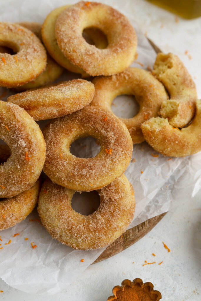 Golden brown donuts on parchment paper sugar and orange zest on top. 