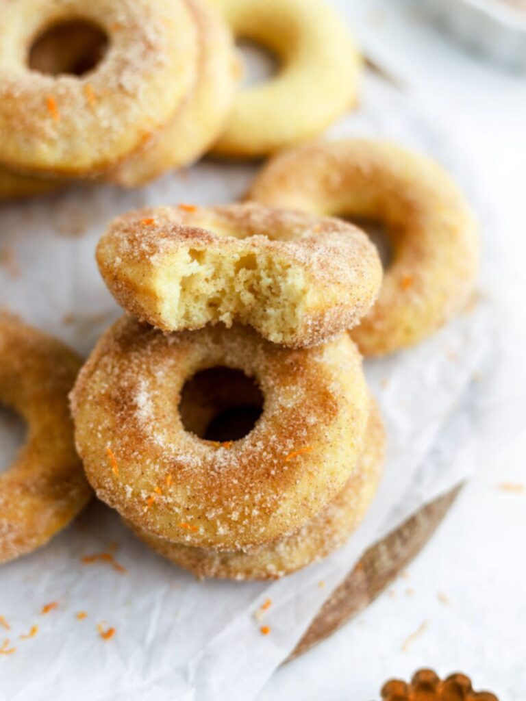 A batch of cinnamon orange donuts with one with a bite taken out of it.