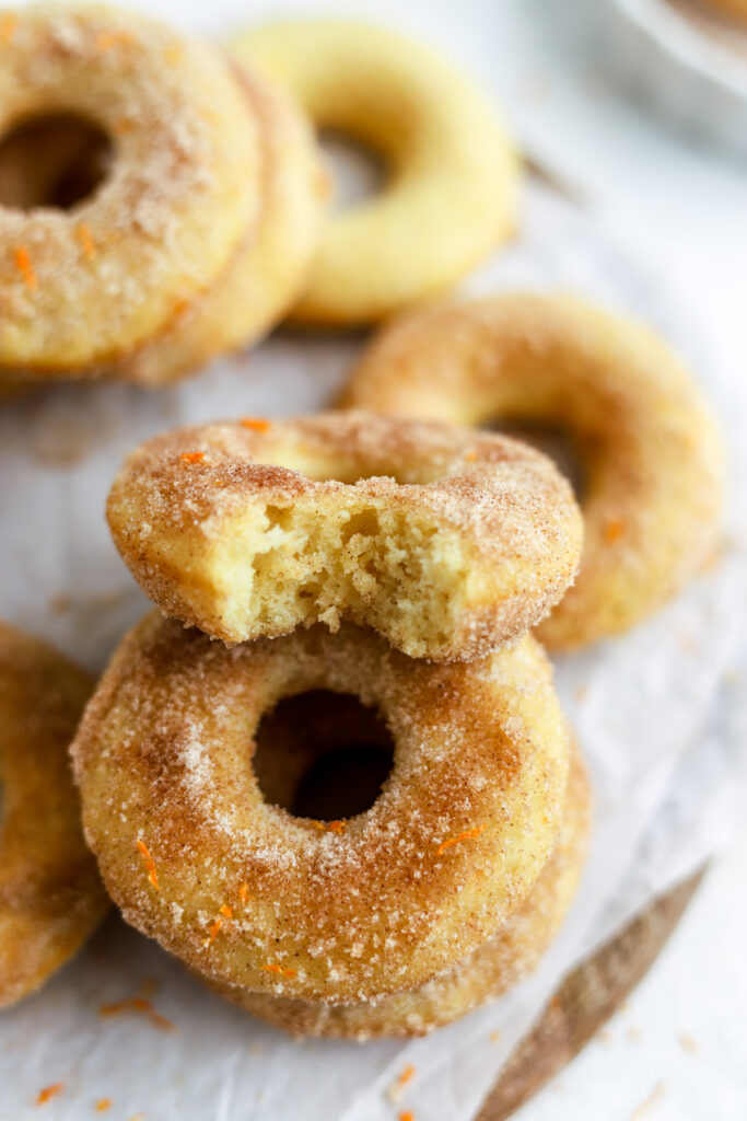 A donut coated with sugar and orange zest and a donut with a bite in it. 