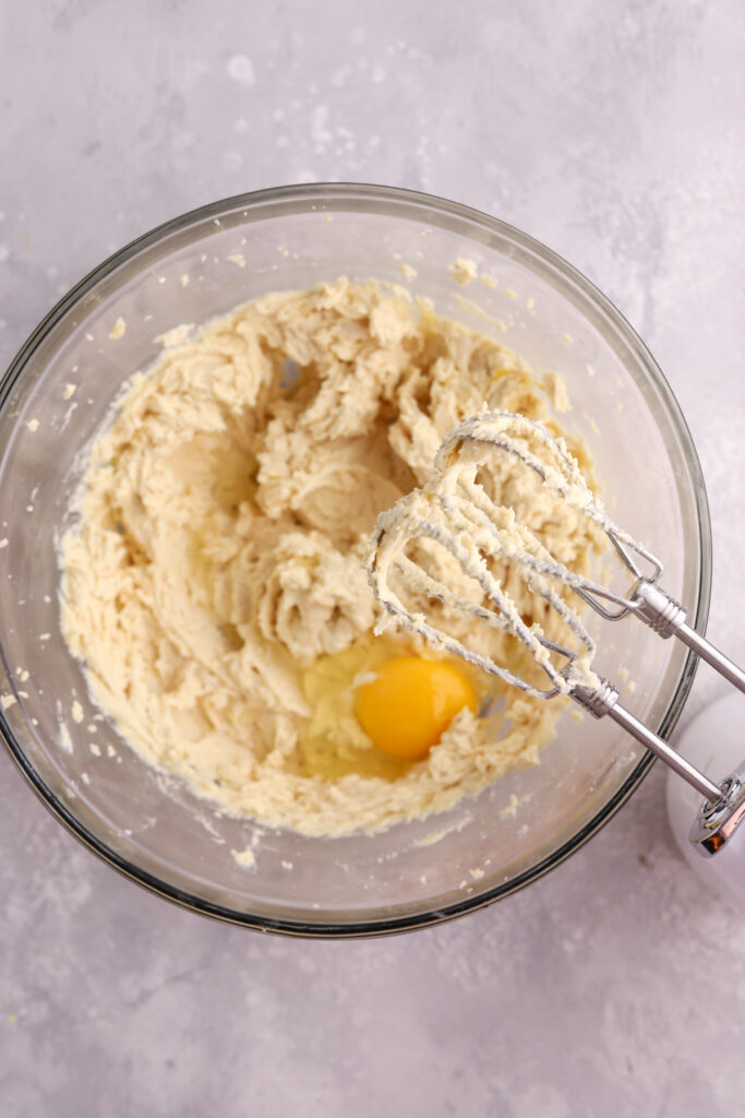 Cookie dough with an egg being added to a mixing bowl. 