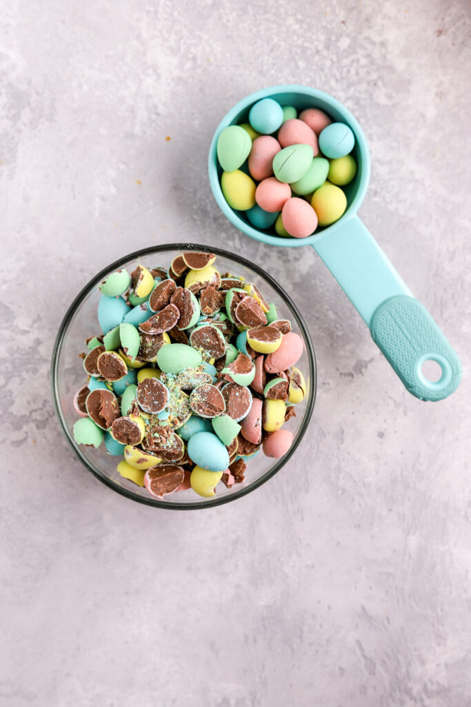 A small bowl and a measuring spoon filled with colorful mini eggs. 