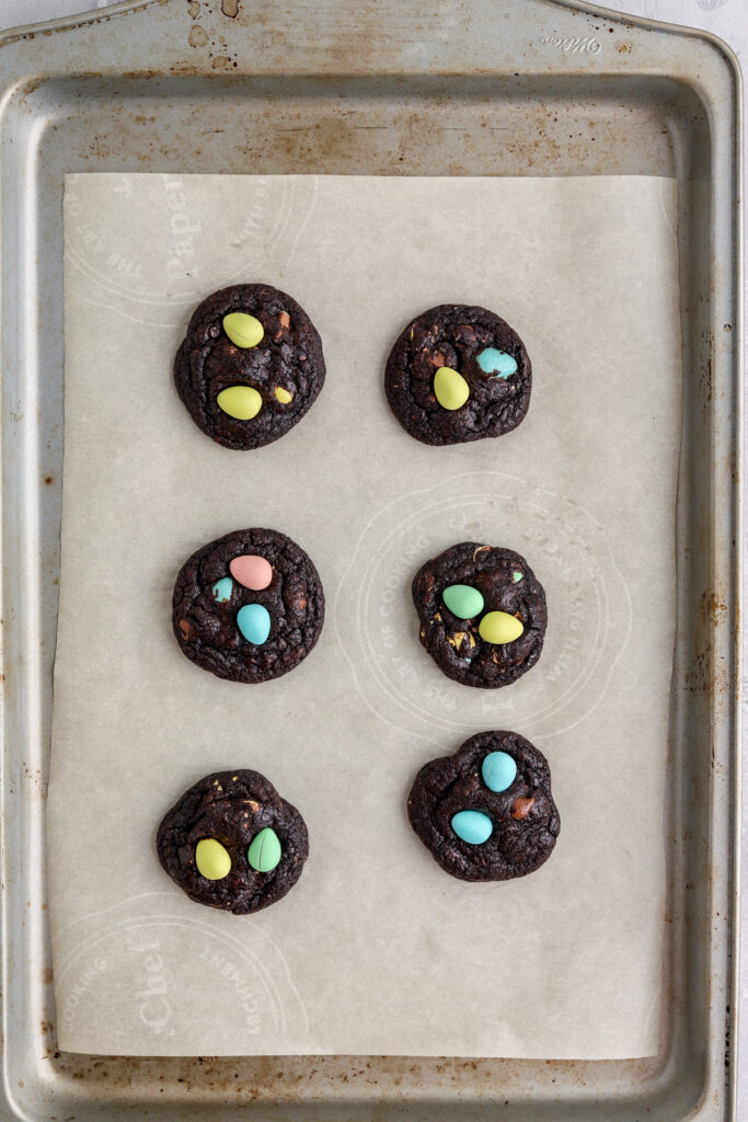 A baking sheet lined with parchment paper with chocolate cookies with mini eggs on top. 
