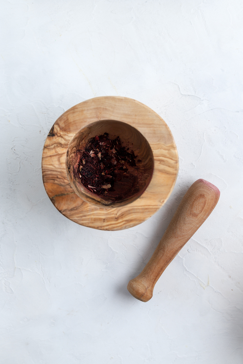 A wooden mortar and pestle with dried hibiscus flowers in it.