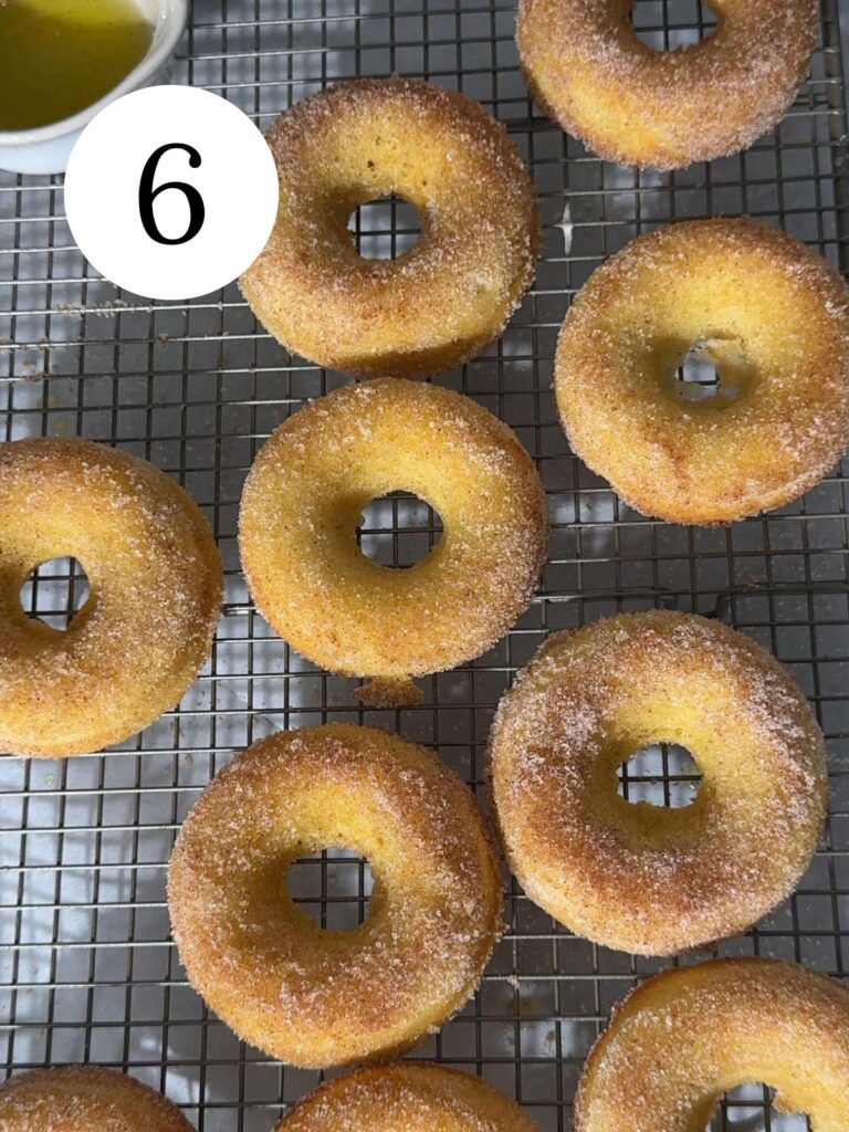 Orange donuts coated with cinnamon sugar on a wire rack.