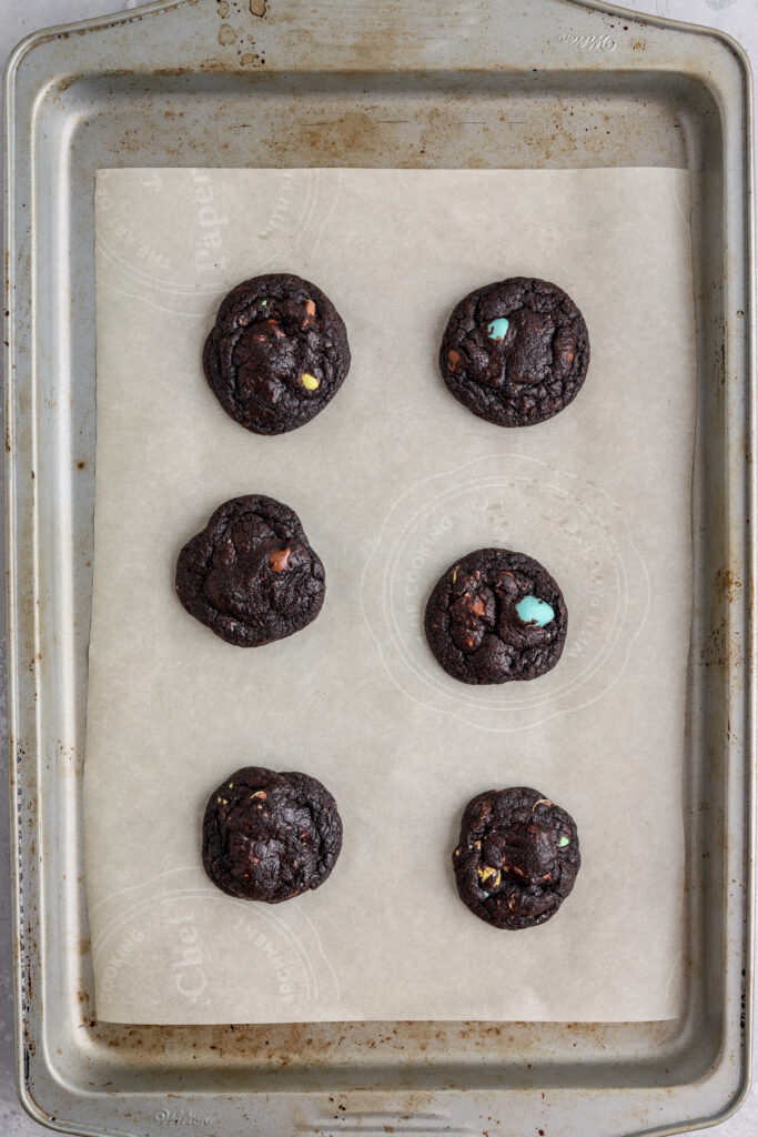 A cookie sheet lined with parchment paper with chocolate cookies on it. 
