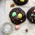Three chocolate cookies with mini eggs and a bowl of salt.