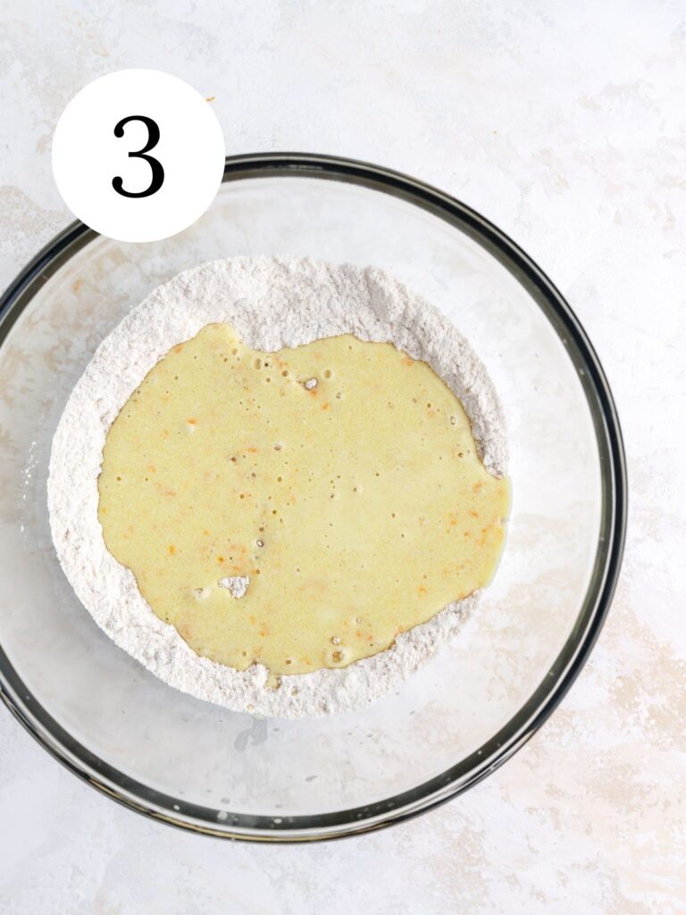 Wet ingredients on top of dry ingredients in a large glass bowl.