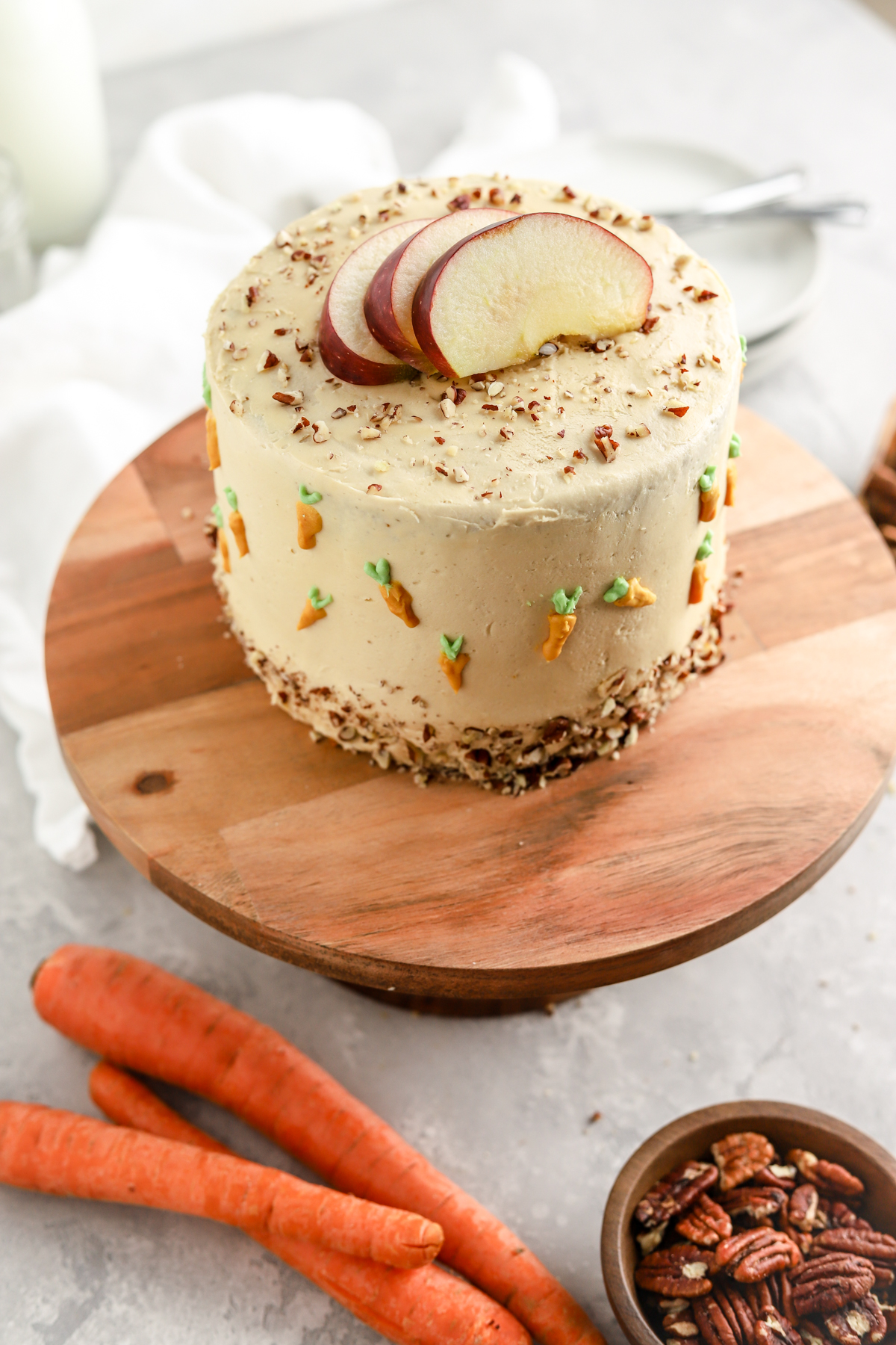 Pumpkin carrot layer cake on a cake stand and some carrots and pecans. 