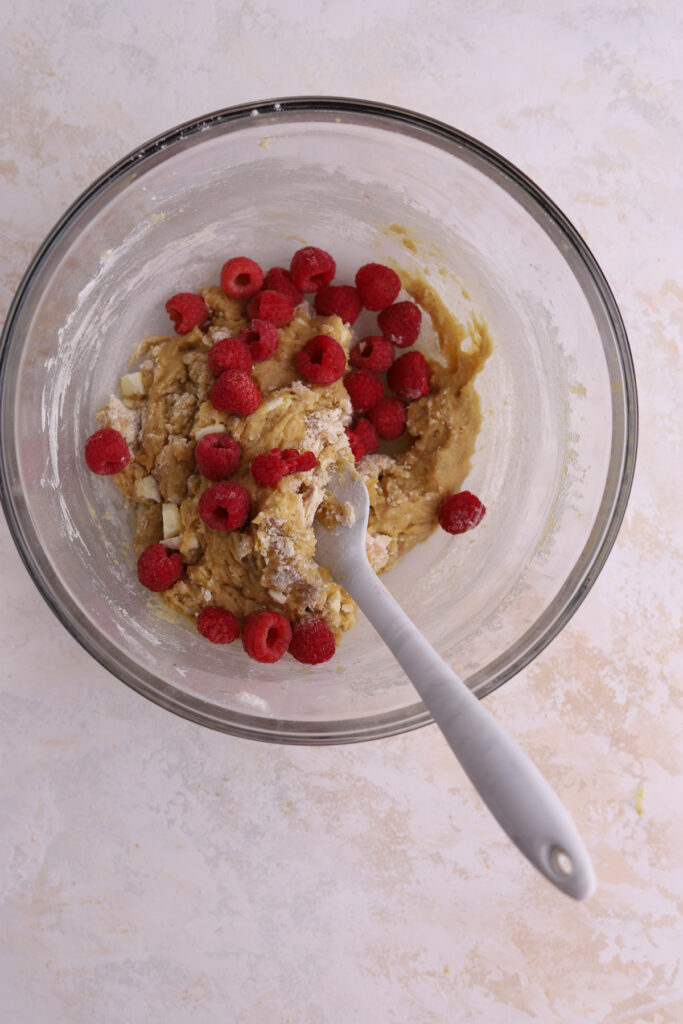 A glass bowl with blondie batter in it and raspberries being mixed in. 