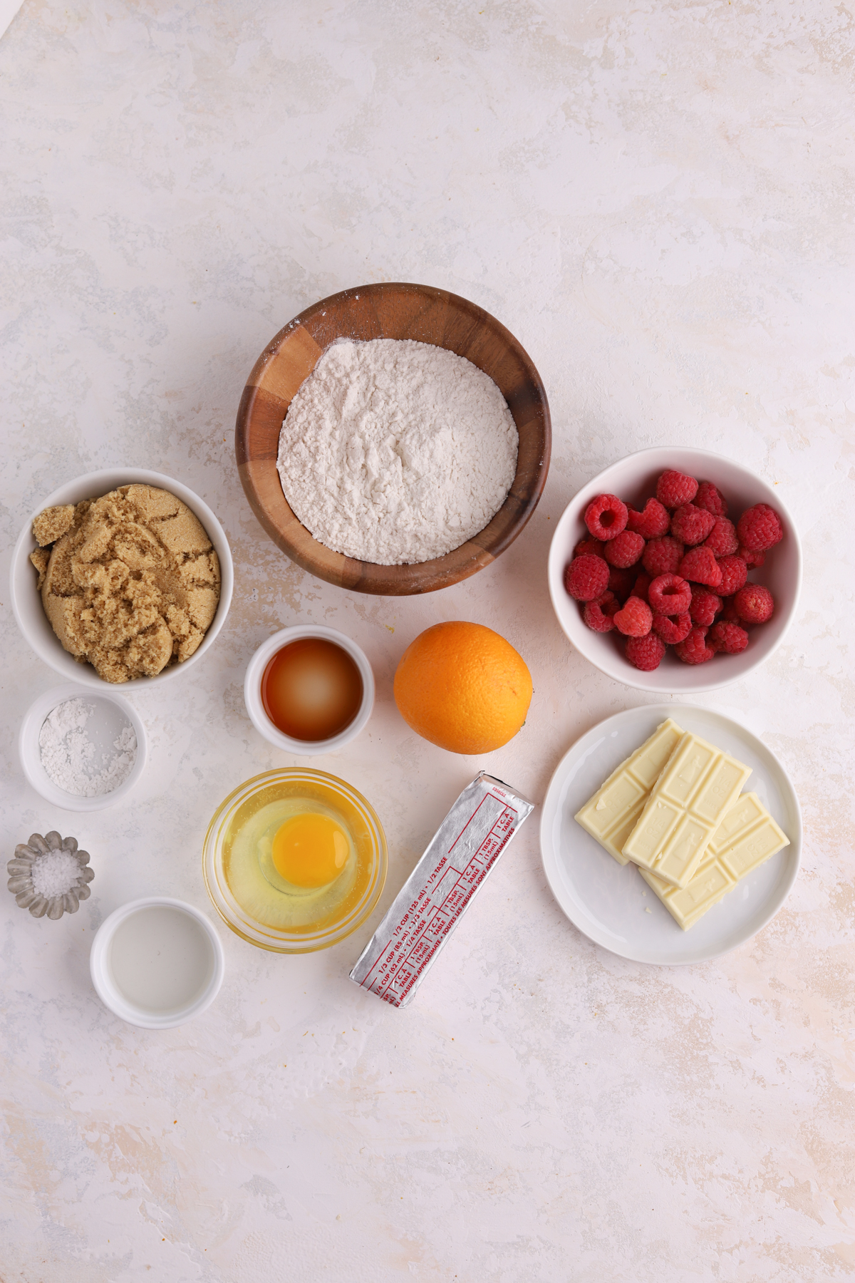 A stick of butter, a bowl of raspberries, some white chocolate and other ingredients. 