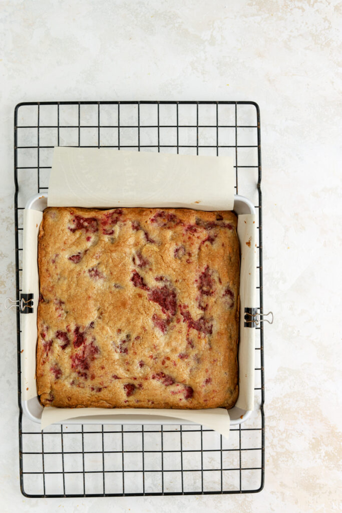 Raspberry blondies in a square pan on a rack.