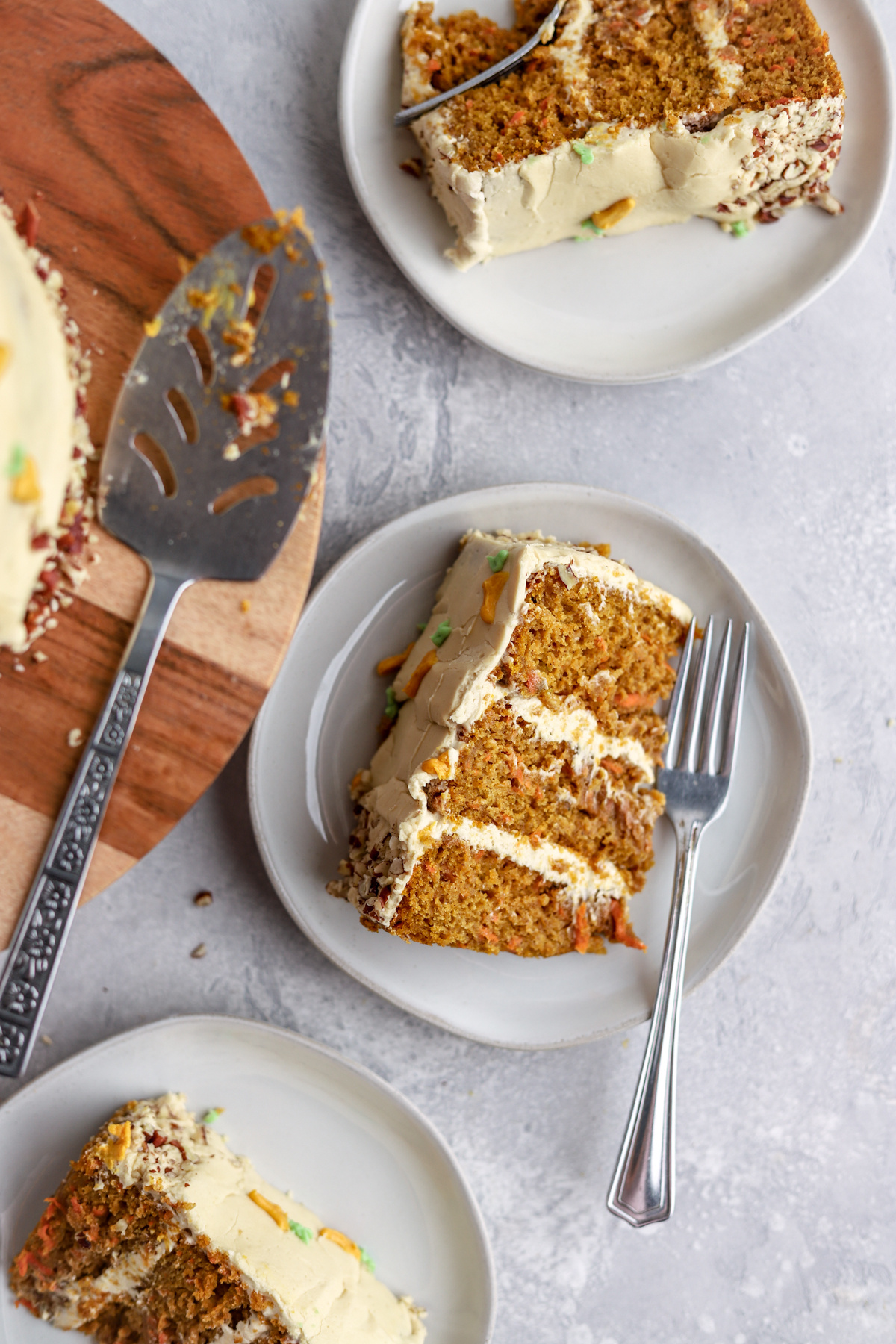 Pumpkin carrot cake slices on plates and a cake server on a cake stand.