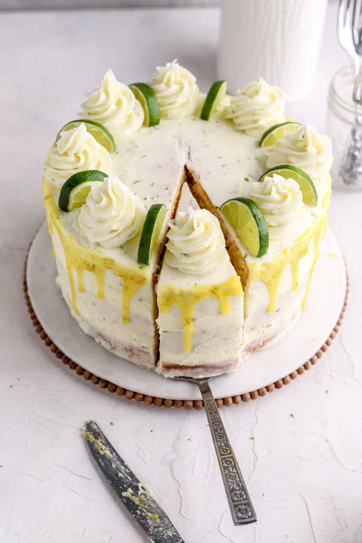 A lime layer cake with a slice cut out out and a jar of silverware. 