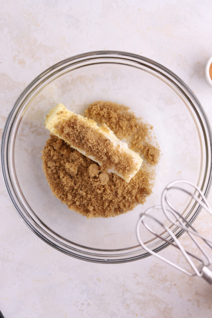 A glass bowl with brown sugar and a stick of butter in it. 