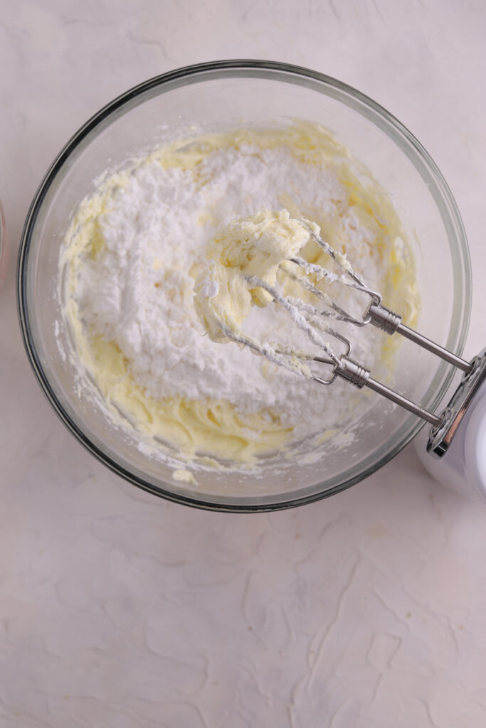 A glass bowl with cake batter being mixed in it and a mixer. 