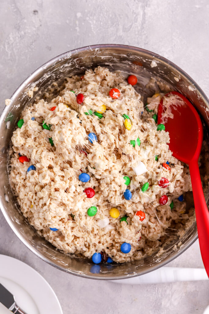 M&M Rice Krispie Treats in a pot with a large red spoon in it. 