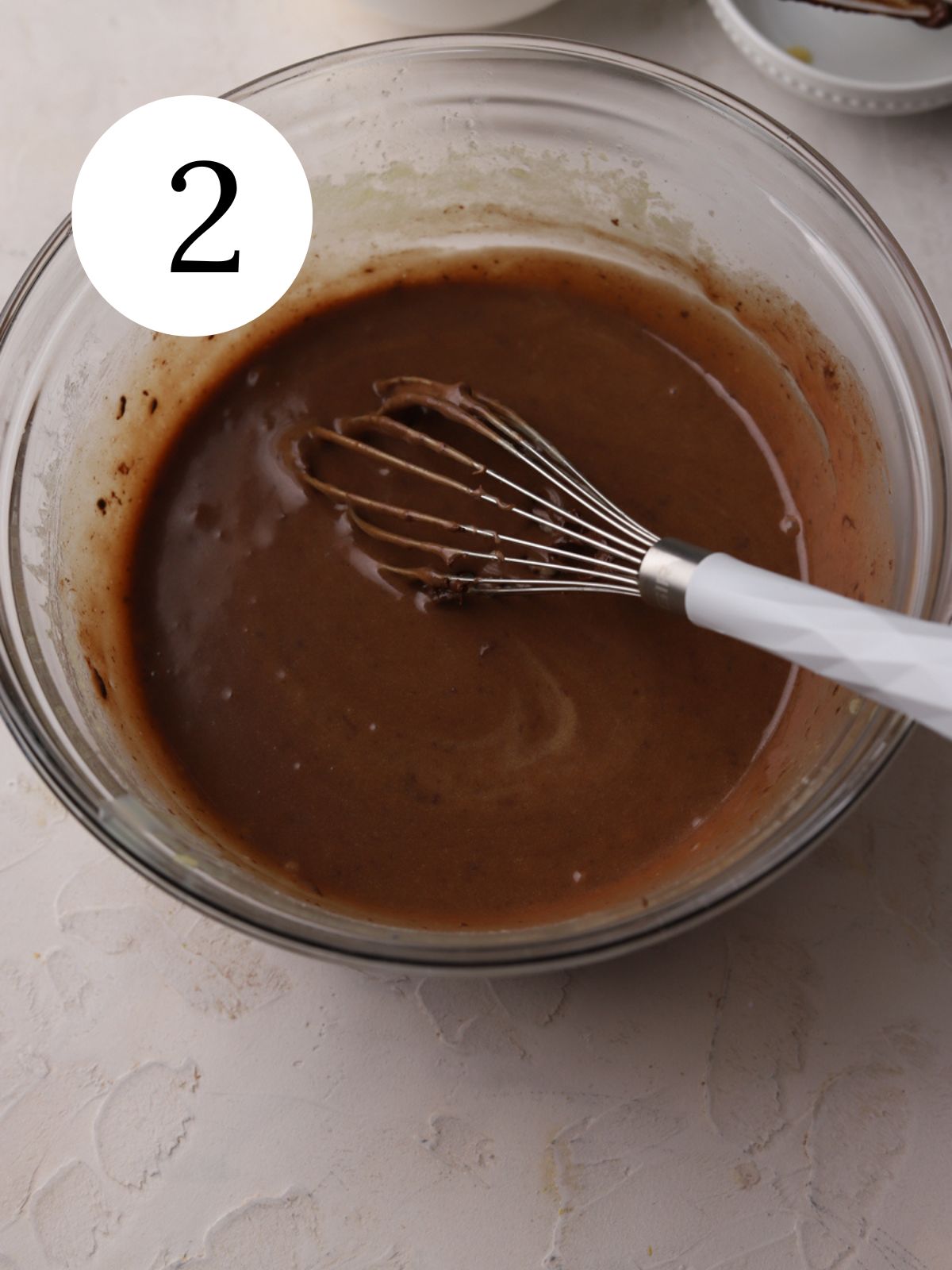 A glass bowl with chocolate batter and a whisk.