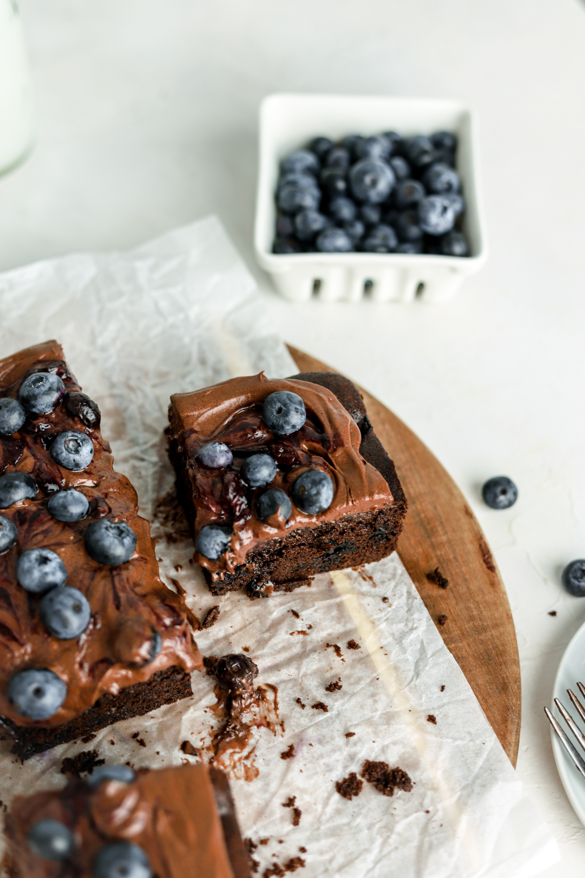 A piece of chocolate cake with blueberries on top and a container of fresh blueberries. 