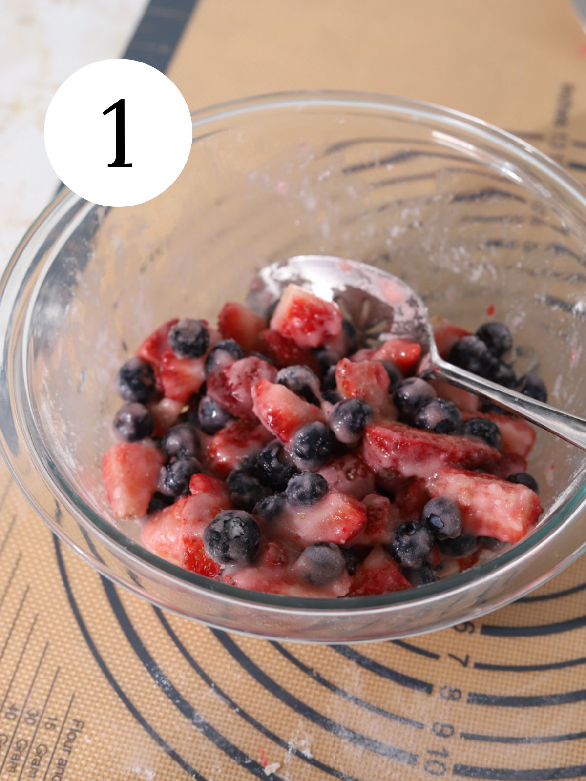 A glass mixing bowl with mixed berries being stirred with a spoon.
