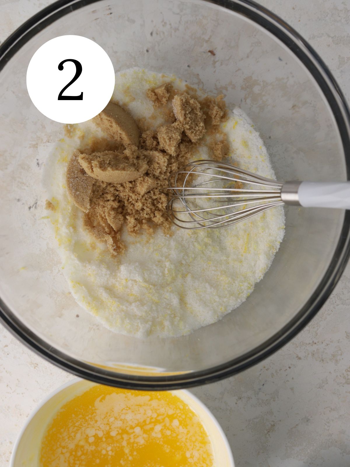 A glass mixing bowl with lemon sugar and brown sugar. 