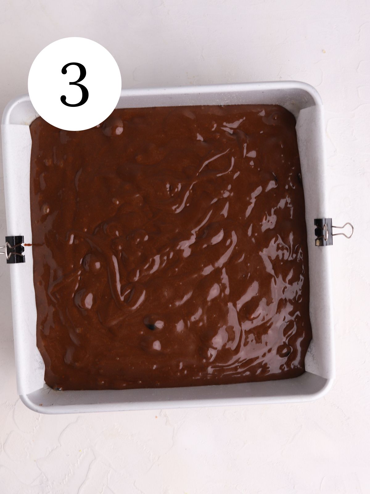 A square baking pan with chocolate cake batter.