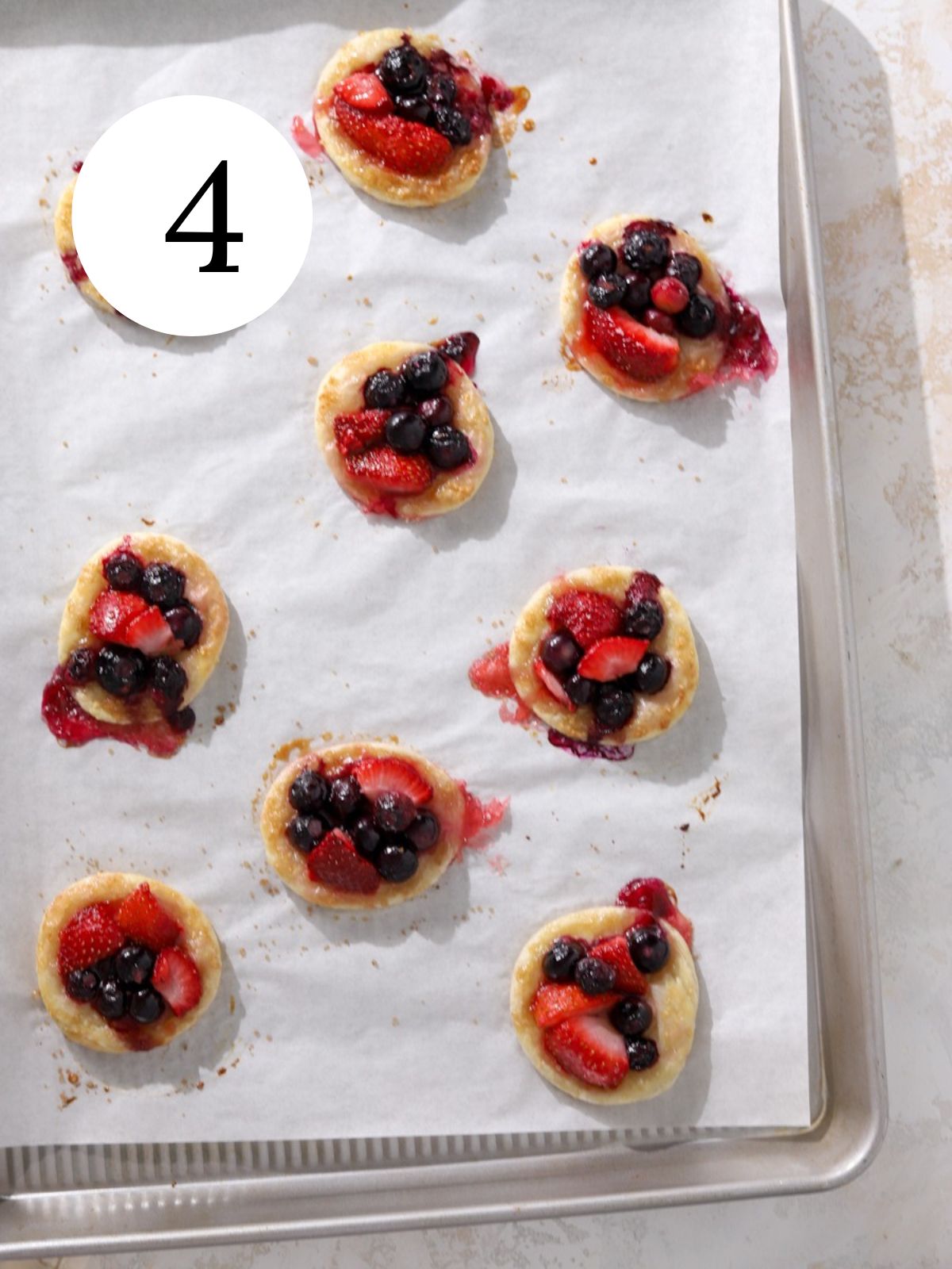 Mini berry pies on a baking sheet lined with parchment paper.