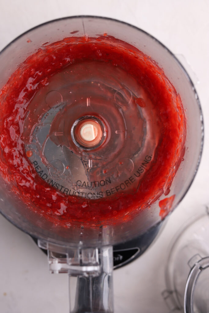 A food processor with pureed cherry pie filling in it. 
